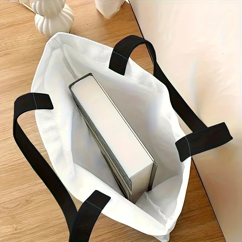 White tote bag with black straps containing a book on a wooden surface
